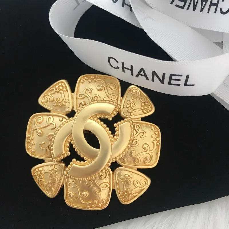 Flower emblem brooch; gold tone, statement design. Full-frame photograph with existing branding.